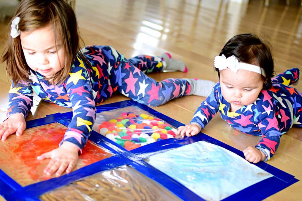 Niños pequeños y bebés jugando con bolsas sensoriales en el suelo