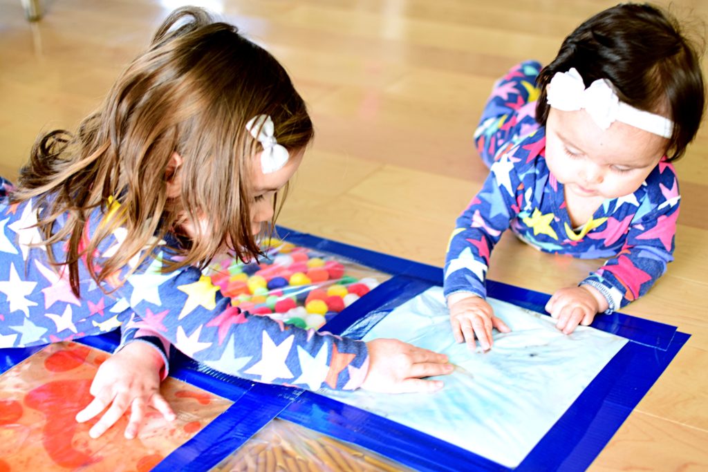 småbarn och flicka som leker med sensoriska väskor på golvet