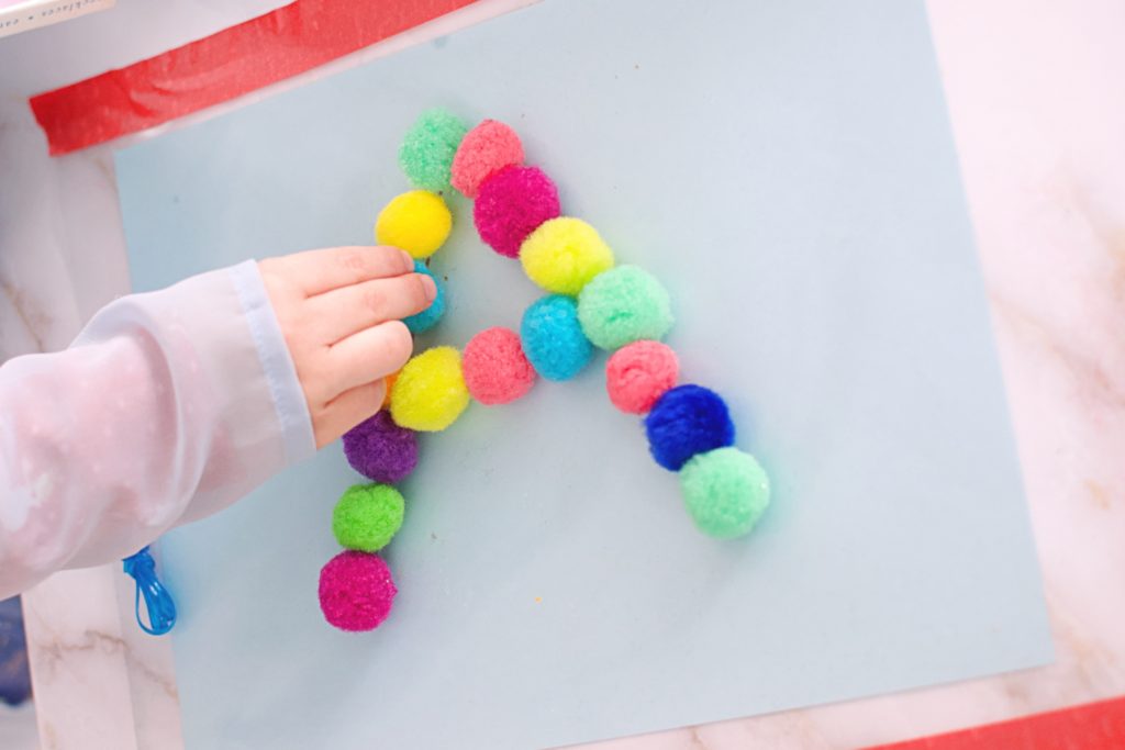 Child practicing their letters by placing pom poms inside the letter A. 
